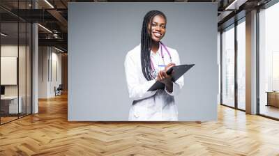 Young african medical intern doctor writing prescription on clipboard isolated on gray background Wall mural